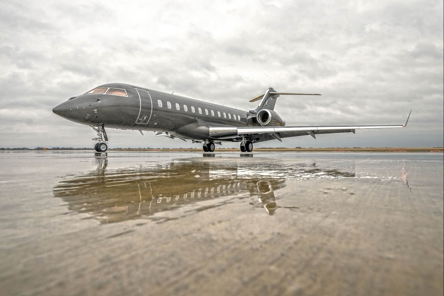 Grey business jet on a wet airport runway beneath overcast skies